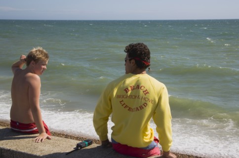 ENGLAND, East Sussex, Brighton, Life guard talking to young boy on the sea wall at Hove.