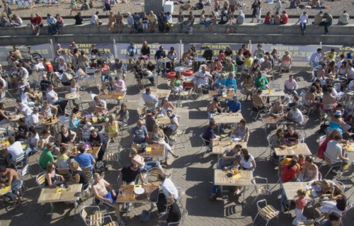 ENGLAND, East Sussex, Brighton, People sat at tables drinking outside the Beach seafront bar.
