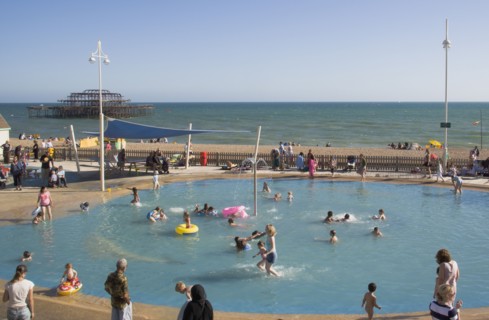 ENGLAND, East Sussex, Brighton, Childrens paddling pool with the ruins of the West Pier behind.