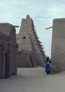 MALI, Tomboctou, Street scene with mud built  Mosque and woman carrying a bowl on her head.