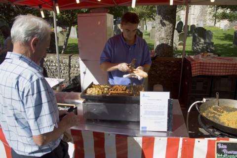 ENGLAND, West Sussex, Shoreham-by-Sea, French Market. Food stall with stallholder cooking sausage
