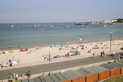 ENGLAND, Dorset, Swanage Bay, Elevated view over beach huts towards busy stretch of sandy beach and