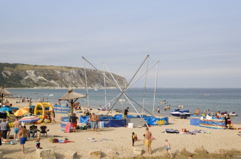 ENGLAND, Dorset, Swanage Bay, Busy colourful sandy beach scattered with inflatables and windbreaks
