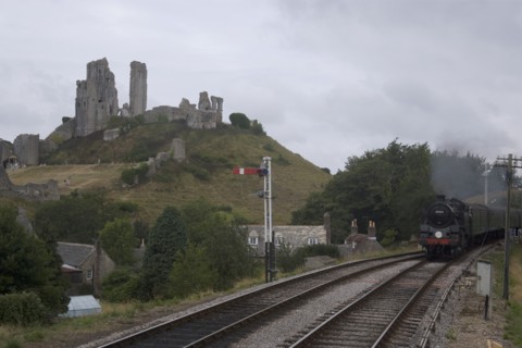 ENGLAND, Dorset, Corfe, Corfe Castle seen behind a railway line with a steam train approaching