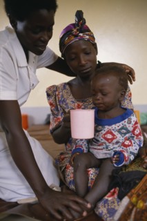 UGANDA, Medical, Nurse comforting mother with child with malaria in hospital in Orukinga refugee
