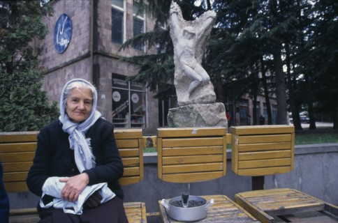 ARMENIA, Idjeran, Elderly woman selling sunflower seeds from wooden seating infront of carved stone