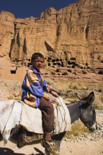 AFGHANISTAN, Bamiyan Province, Bamiyan , Boy on donkey infront of caves in cliffs near empty niche