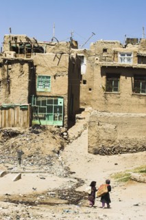 AFGHANISTAN, Ghazni, "Children walk with sacks over their shoulders toward houses inside the