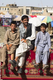 AFGHANISTAN, Kabul, Money changer sits on rug on walls of Kabul river with street boys