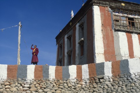 NEPAL, Mustang, Tsarang Gompa, "Tibetan Buddhist monk looking out from monastery terrace, shielding