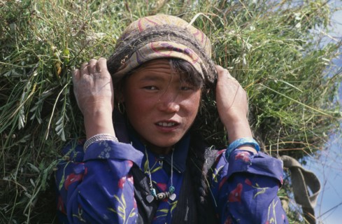 NEPAL, Mustang, Lo Manthang, Portrait of young girl carrying load of harvested grasses supported by