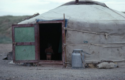 MONGOLIA, Architecture, Young child standing inside open doorway of yurt wearing just a jumper and
