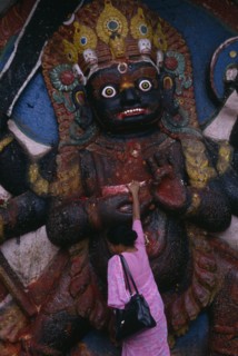 NEPAL, Kathmandu, Woman making offerings at the Kala Bhairab or black Shiva in Durbar Square