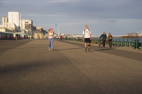 ENGLAND, East Sussex, Brighton, Woman jogging with man rollerblading on the seafront promenade.
