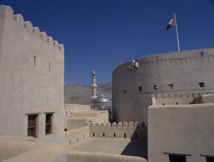 UAE, Oman, Nizwa, Minaret and blue and gold domed roof of mosque seen from fort walls with barren