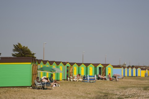 ENGLAND, West Sussex, Littlehampton, Green and yellow beach huts on shingle beach with sunbathers