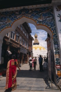 NEPAL, Kathmandu, A woman wearing a red sari walking through ornate Gateway towards Bodhnath