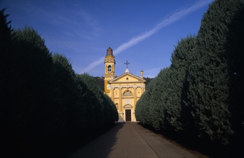 ITALY, Lombardy, Yellow and white exterior facade of small church with bell / clock tower at side