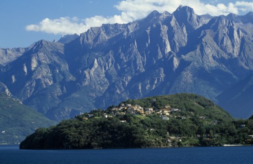 ITALY, Lombardy, Lake Como, View across lake towards distant tree covered peninsula and the Abbey