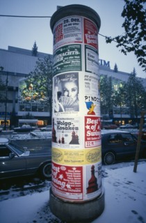 GERMANY, Berlin, Poster pillar along Kurfurstendamm commercial street in West Berlin at winter time