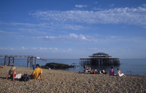 ENGLAND, East Sussex, Brighton, Groups of people sitting on the beach by the ruined West Pier in