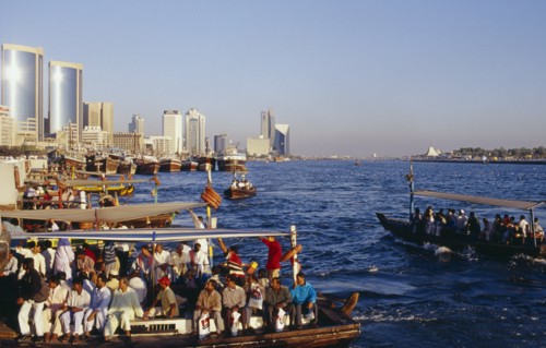 UAE, Dubai, Dubai Creek, Abra water taxis with passengers on Creek with city skyline beyond.