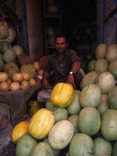 BANGLADESH, Dhaka, Man selling durians and melons in fruit market.
