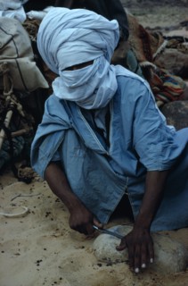 ALGERIA, Sahara Desert, Tuareg, "Tuareg man sharpening tool on rock, wearing blue taguelmoust