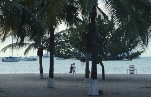 VENEZUELA, Estado Anzoategui, Puerto La Cruz, Couple on beach looking out over water and moored