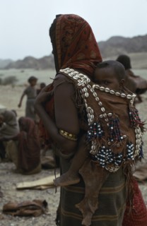 ETHIOPIA, Danakil , People, Mother carrying baby on her back in leather sling decorated with beads