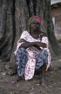 SENEGAL, People, Portrait of woman seated at base of tree trunk wearing fabric of different printed