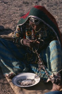 INDIA, Rajasthan, People, Kalbelia gypsy woman in traditional dress stringing beads.