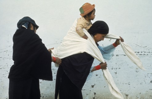 20088957 ECUADOR Imbabura Otavalo Indian woman helping another wrap young child in blanket sling on her back at Otavalo market.
