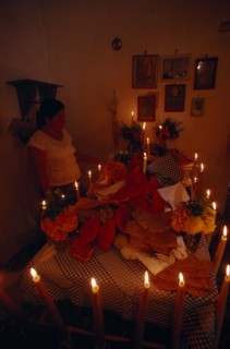 MEXICO, Acatlan, Woman lighting candles around altar for Day of the Dead covered with food and