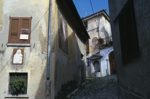 ITALY, Lombardy, Arcumeggia, Narrow cobbled street with fresco decoration and plaster relief of the