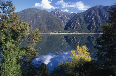 ITALY, Lombardy, Lake Iseo, Lago d’Iseo.  Trees and mountain landscape reflected in still surface