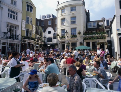 ENGLAND, East Sussex, Brighton, The North Lanes. East Street. People eating and drinking at tables