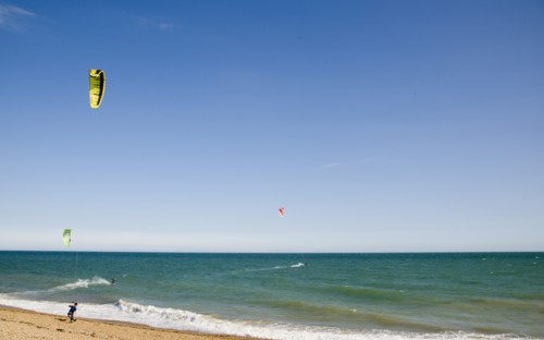 ENGLAND, West Sussex, Lancing, Kite Surfers on sea next to shingle beach in the summer with blue