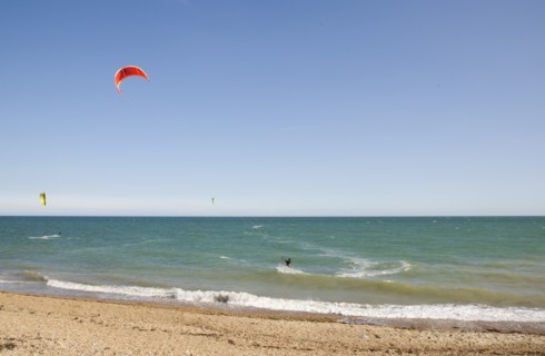 ENGLAND, West Sussex, Lancing, Kite Surfers on sea next to shingle beach in the summer with blue