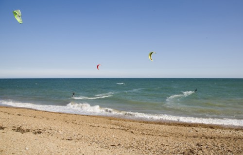 ENGLAND, West Sussex, Lancing, Kite Surfers on sea next to shingle beach in the summer with blue