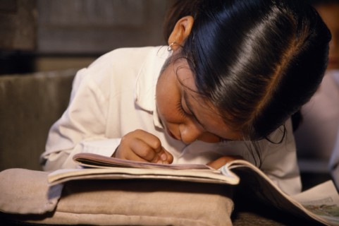 NEPAL, Dhulikhel, "Little girl, head bent forward in concentration over exercise books in primary