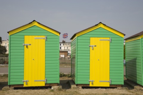 ENGLAND, West Sussex, Littlehampton, Green and yellow beach huts next to promenade with a Union