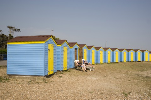 ENGLAND, West Sussex, Littlehampton, A crescent of blue and yellow beach huts with a couple