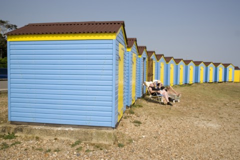 ENGLAND, West Sussex, Littlehampton, A crescent of blue and yellow beach huts with a couple