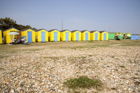 ENGLAND, West Sussex, Littlehampton, A crescent of  yellow and blue beach huts with sunbathers on