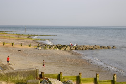 ENGLAND, West Sussex, Selsey, Children playing with bucket and spade on sandy beach next to sea