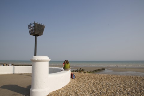 ENGLAND, West Sussex, Bognor Regis, Two young women sitting on a white wall facing each other