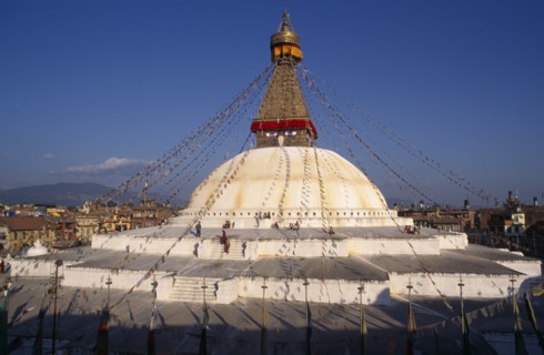 20086659 NEPAL Kathmandu Valley Bodhnath People circumambulate giant central stupa hung with prayer flags and painted with eyes of Buddha.  Town spread out beyond.