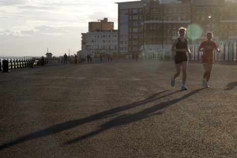 ENGLAND, East Sussex, Brighton, Silhoetted joggers on the seafront at Hove Lawns.