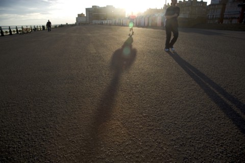 ENGLAND, East Sussex, Brighton, Silhoetted joggers on the seafront at Hove Lawns.